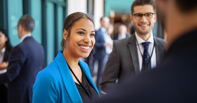 Woman in blue blazer talking with two men in a crowded office hallway. 